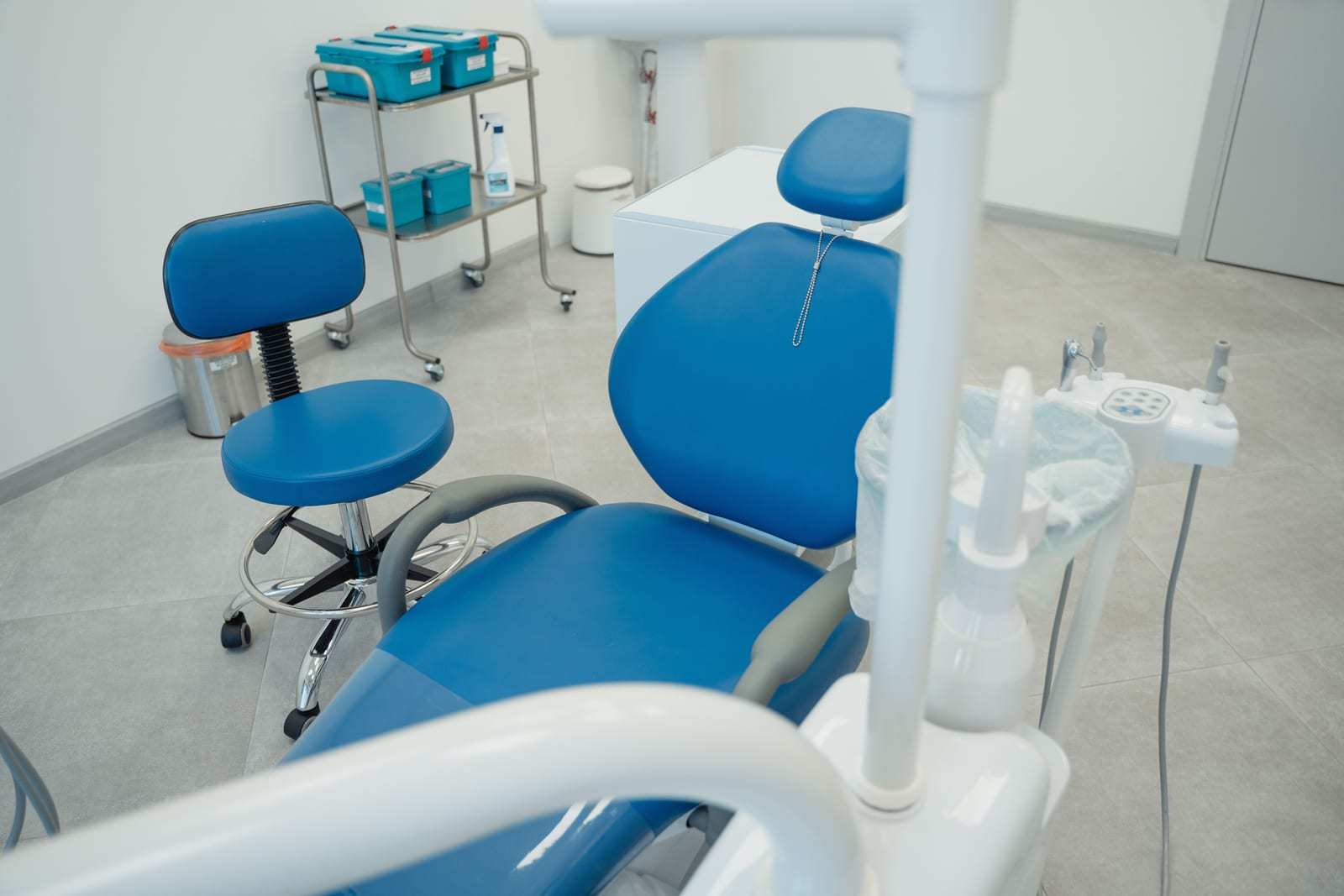 An empty dental treatment room with a blue chair and stool