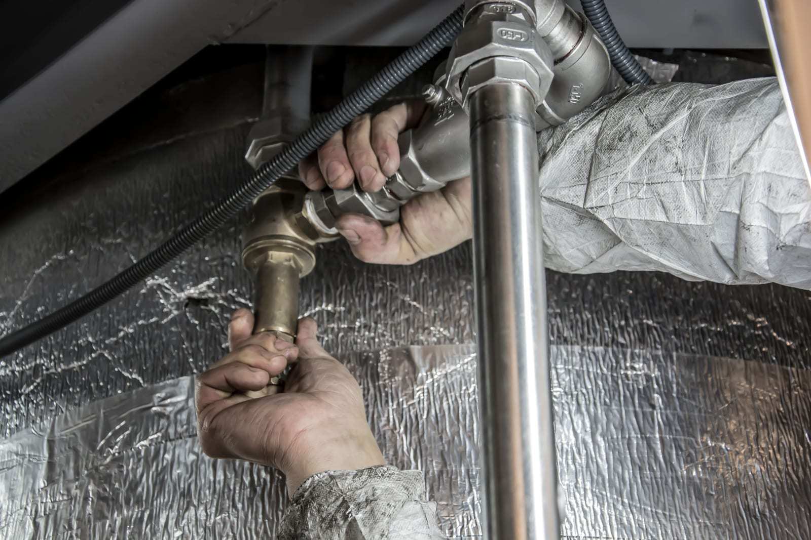 Two hands tightening a brass fitting on a steel water pipe