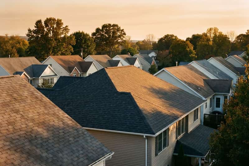 Suburban rooftops at sunset with one newly shingled roof in front